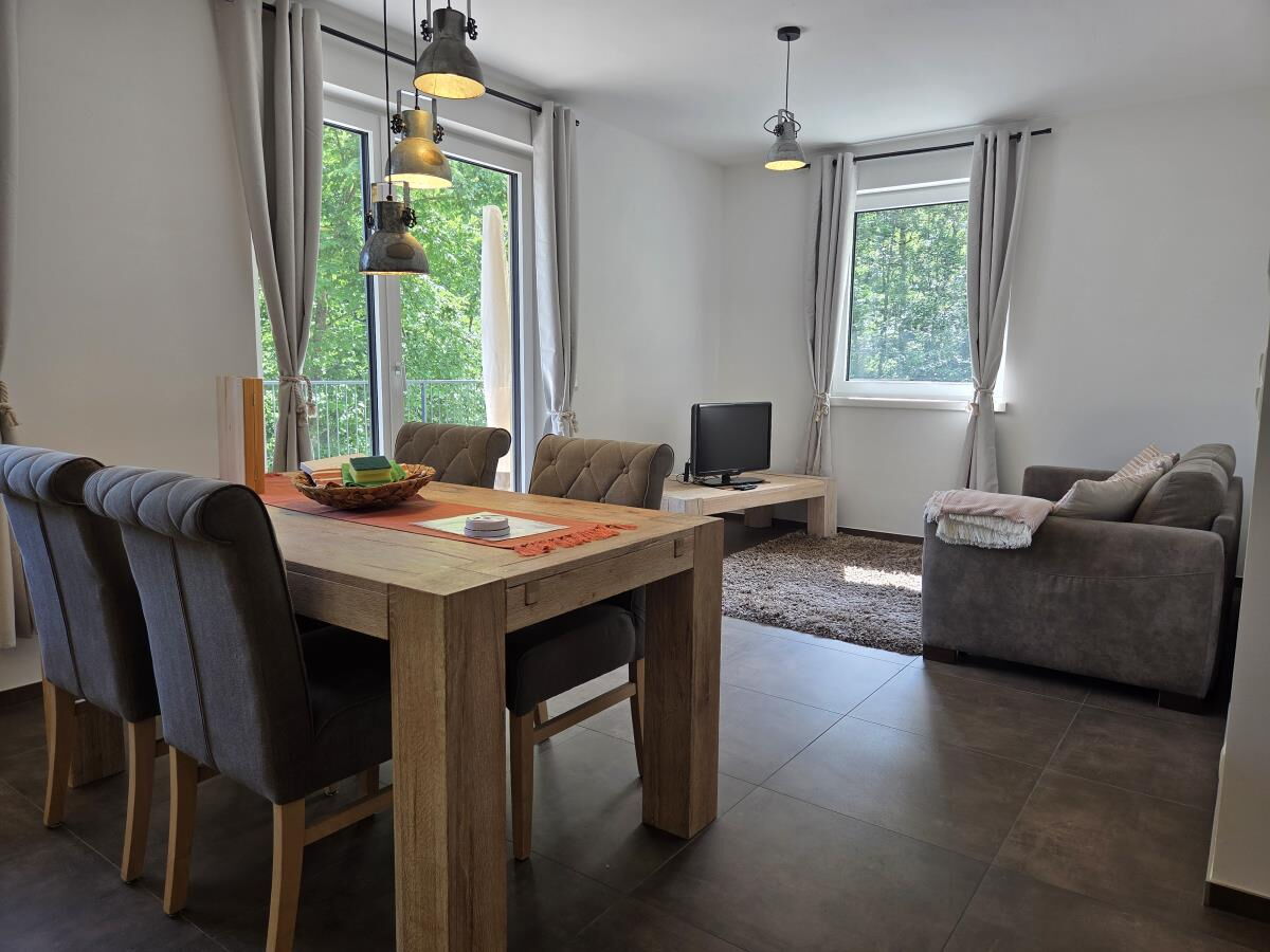 Living area of the Waldsicht holiday apartment near the Karwendel with a large wooden table, sofa and two windows facing the greenery
