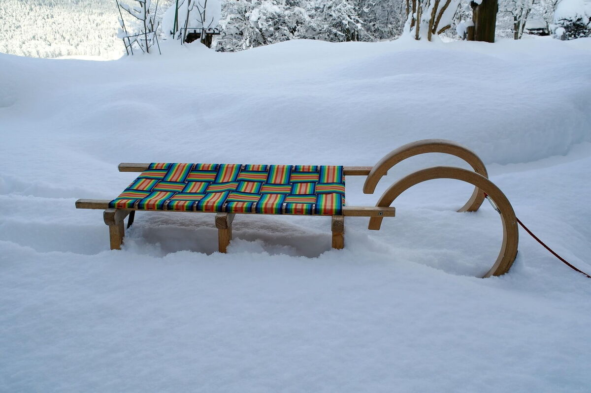 Alte Holzrodel steht im tiefen Schnee vor verschneiten Bäumen am Hochrindl
