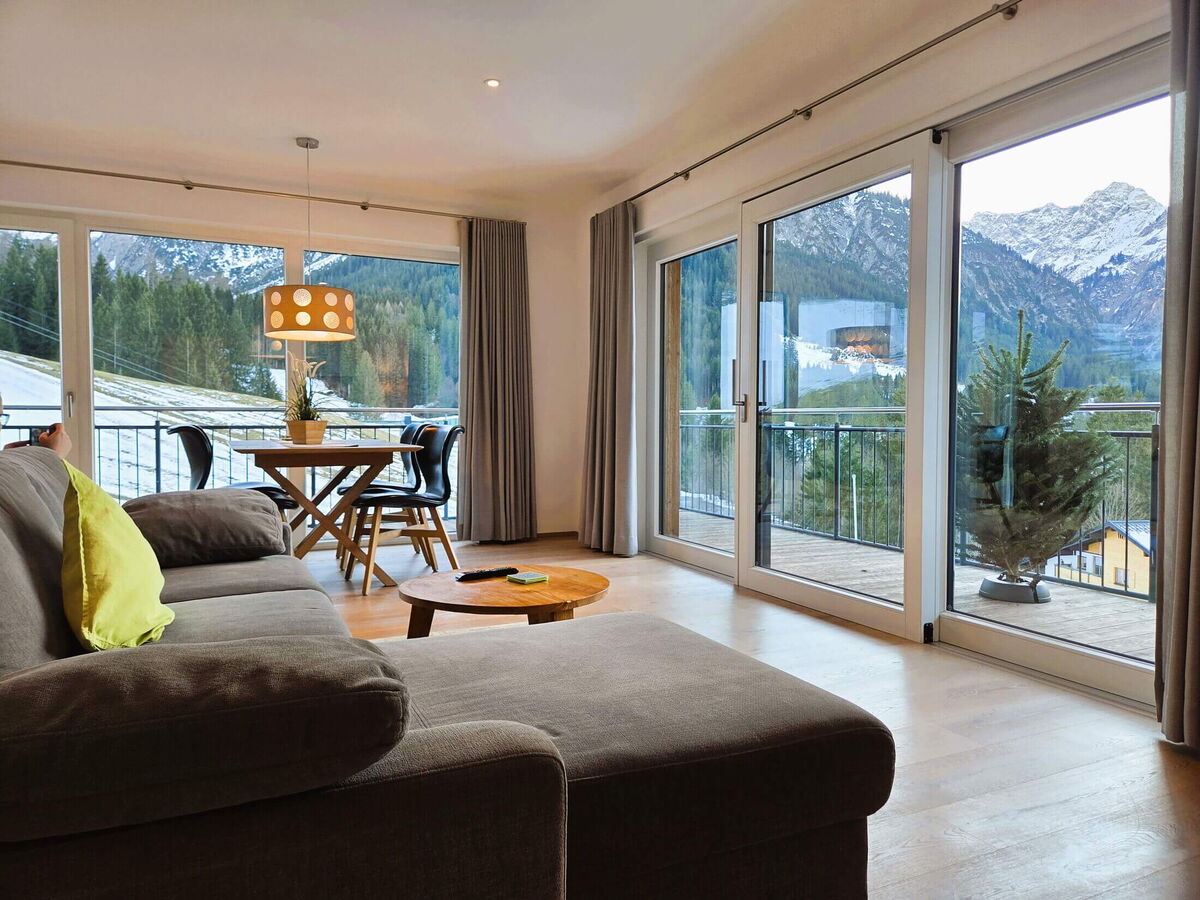 Wohnzimmer mit Ecksofa, Esstisch und bodentiefer Fensterfront zum Süd-Balkon in der Bergwiese-Luxuslodge Zwölferkopf, Luxuslodge für 6 Personen im Kleinwalsertal