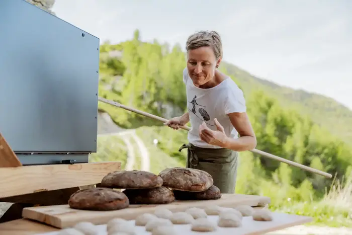 Bäuerin holt frisch gebackene Brotlaibe mit dem Brotschieber aus dem Holzbackofen im Freien