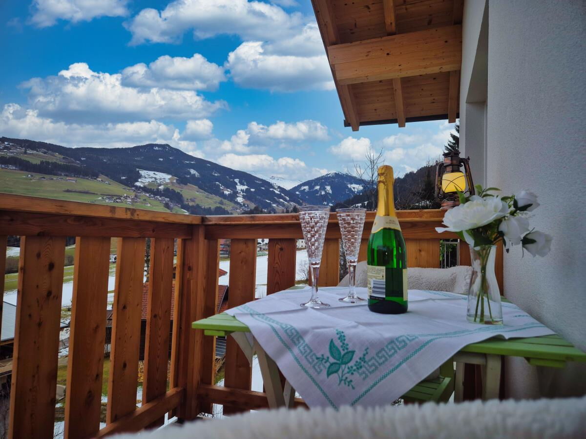 Gedeckter Tisch mit Sekt und Blumen auf dem Holzbalkon der Ferienwohnung Sternenhimmel am Kolsassberg, Blick auf die Berge der Tuxer Alpen