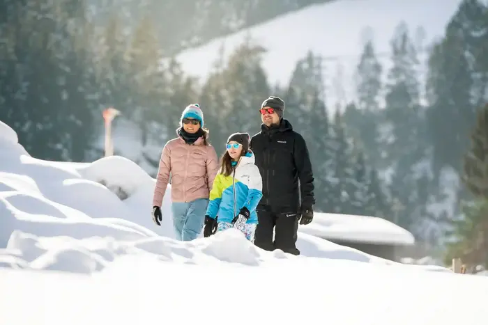 A family winter walking on the cleared path through the deeply snow-covered landscape
