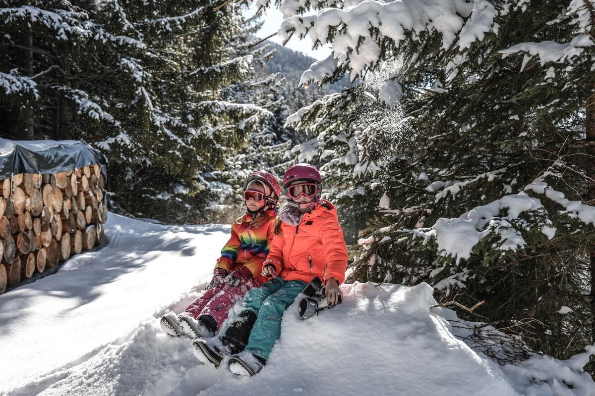 Zwei Kinder rodeln auf dem verschneiten Waldweg in den Tuxer Alpen, Winterspaß für Familien rund um das Kochhäusl
