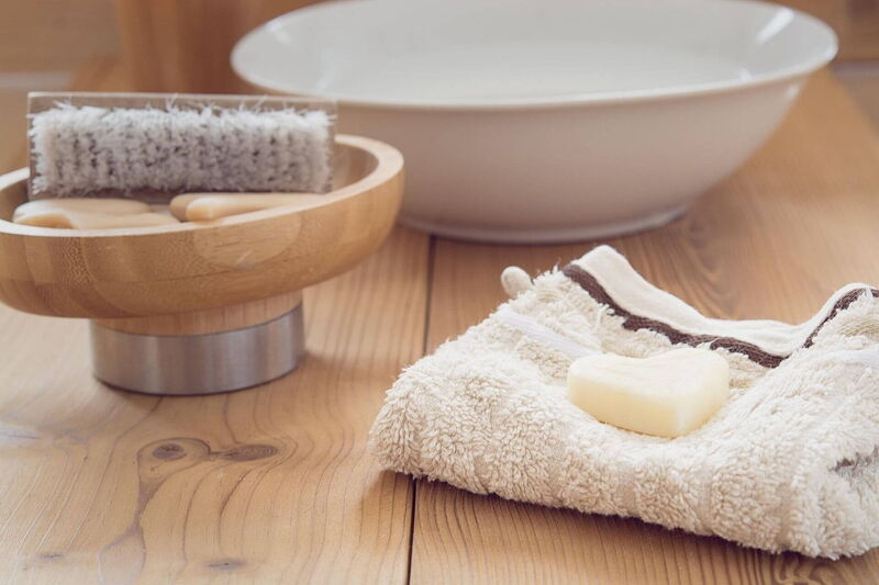 Im Badezimmer auf der Holzablage ist eine Schüssel mit Nagelbürste, ein Waschlappen mit Herzseife darauf liegend und einer Keramikschüssel mit Wasser schön angerichtet..
