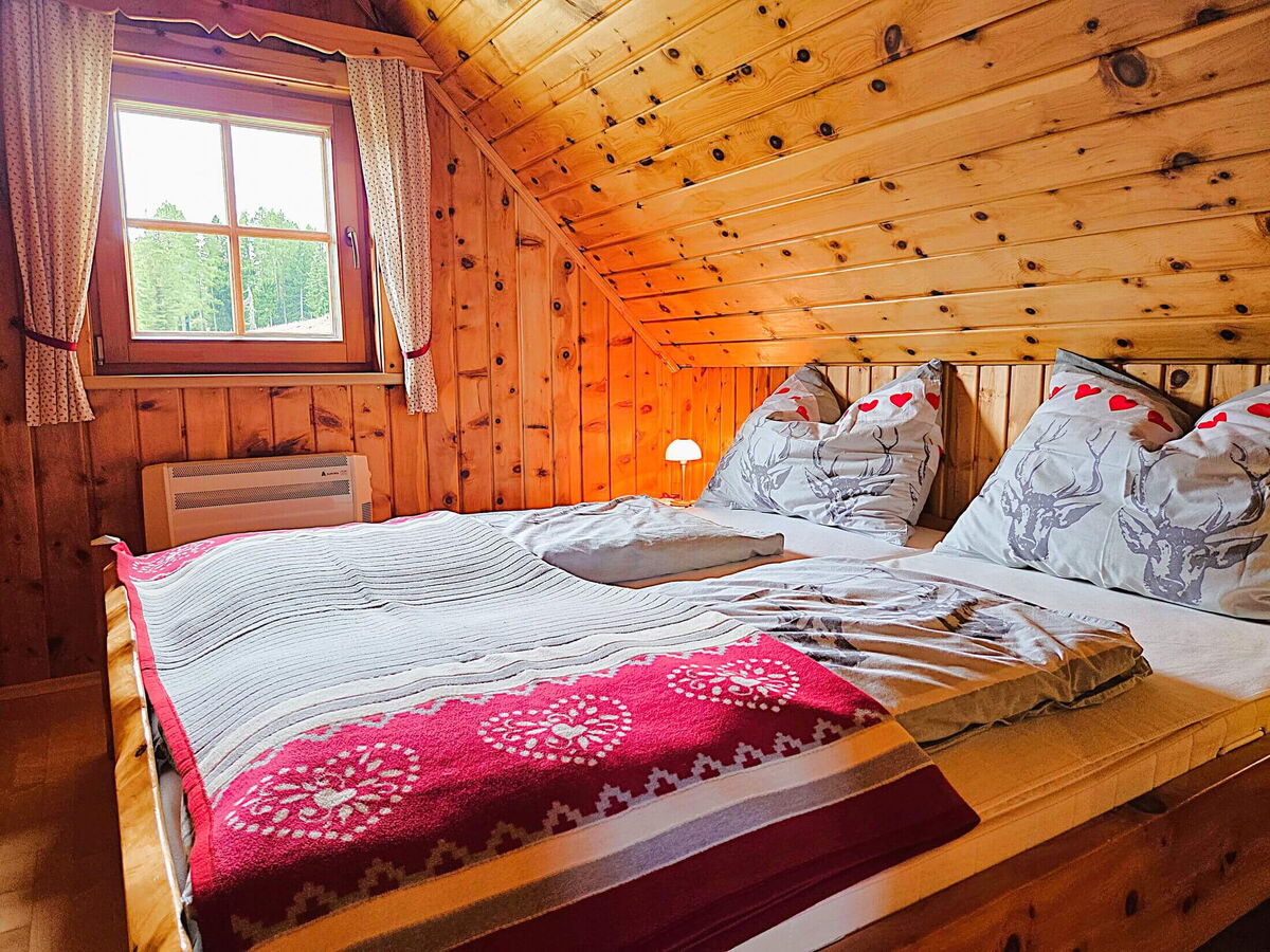 Schlafzimmer der Pietschacher Almhütte mit Doppelbett am Fenster, Zirbenwänden und Blick auf die Almwiese