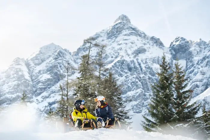 Two tobogganists on the snowy run in front of the striking rock face in the winter forest