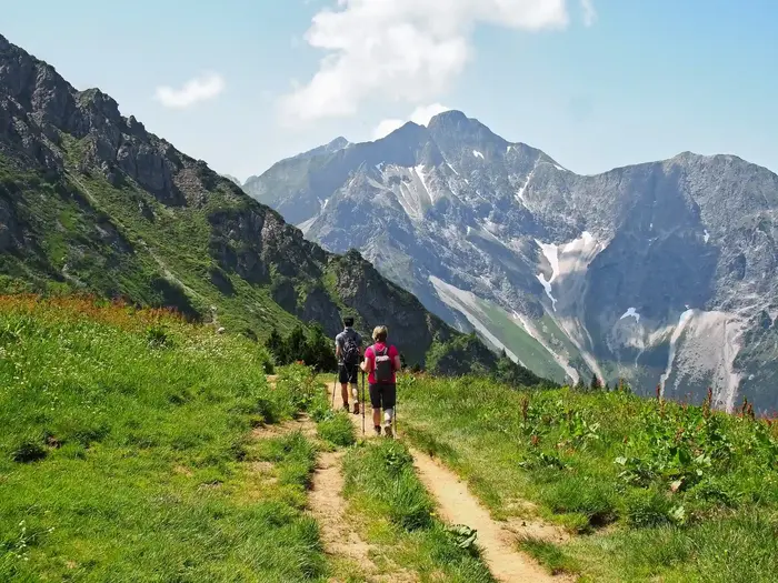 Zwei Wanderer auf schmalem Wiesenpfad Richtung Felsgipfel in den Bergen Vorarlbergs
