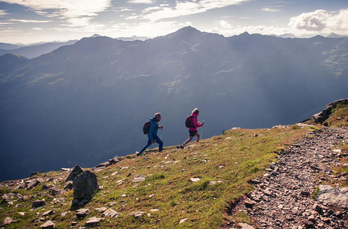Zwei Wanderer gehen im Morgenlicht über einen Grat hoch über dem Inntal in Tirol