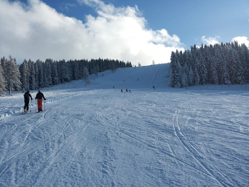 Two ski tourers ascending a wide snow-covered slope in the Nock Mountains