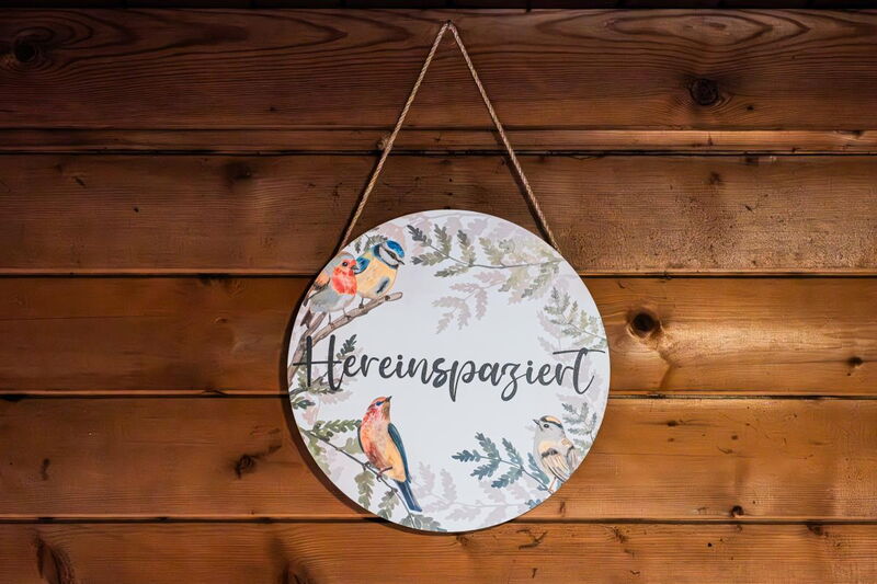 Wooden sign reading „Hereinspaziert“ – come on in – with a bird motif on the larch wall of the Waldhüttl