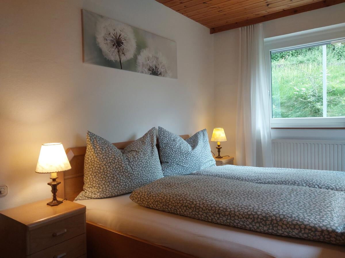 Schlafzimmer der Ferienwohnung Sonnseitn Karwendel mit Doppelbett, zwei Nachttischlampen und Fenster ins Grüne