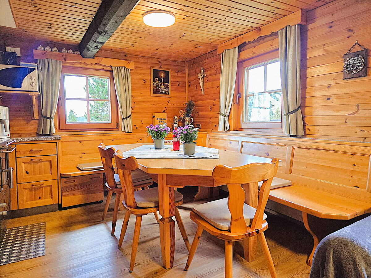 Esszimmer der Pietschacher Almhütte mit großem Holztisch, Stühlen, Eckbank und zwei Fenstern