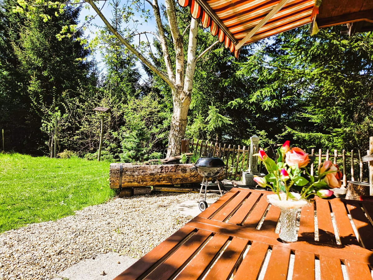 Holzterrasse mit Tisch, Blumenstrauß und Grill vor dem Kochhäusl am Wattenberg, Berghütte in Alleinlage mit Wiese ringsum