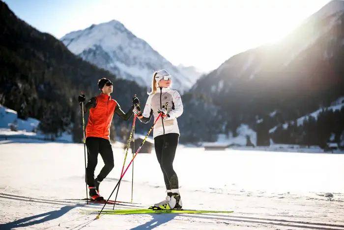 Two cross-country skiers on the track in the snow-covered valley floor against the light