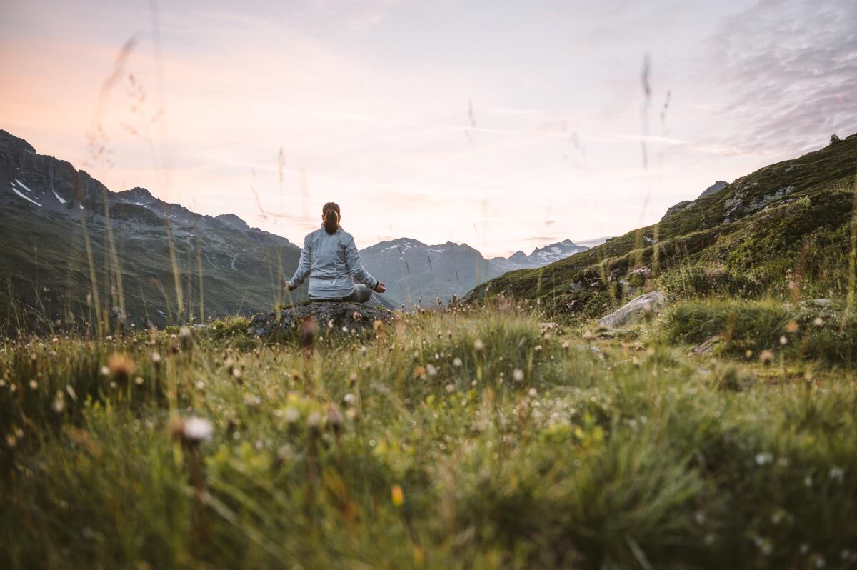 Person sitzt allein auf der Almwiese im Abendlicht nahe der Zarze Almhütte, Stille im Nationalpark Hohe Tauern
