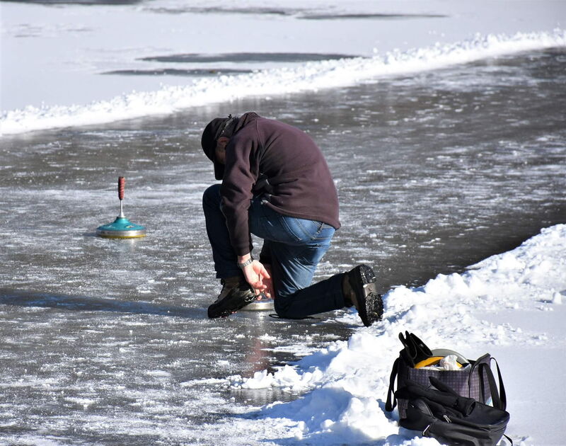 Man kneeling on the frozen lake placing his ice stock on the ice during a game of Bavarian curling
