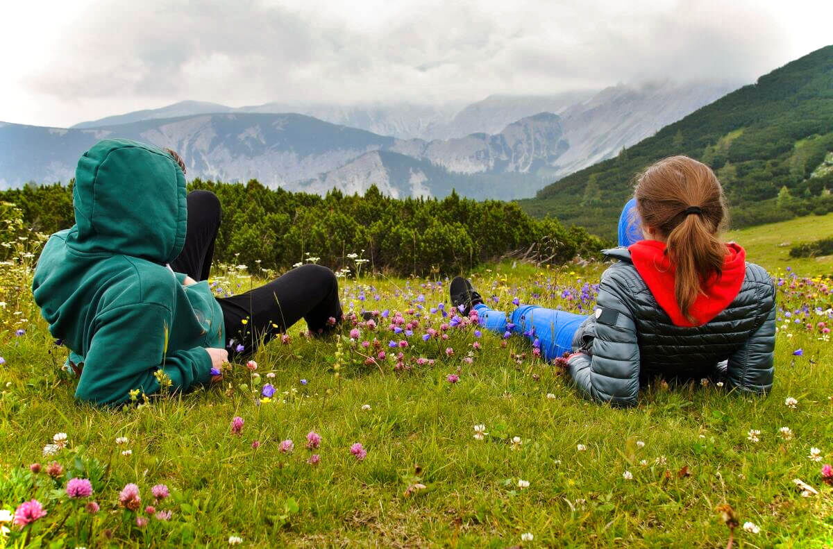Wanderer machen gemütlich Pause auf einer Almwiese mit Bergpanorama in Niederösterreich.