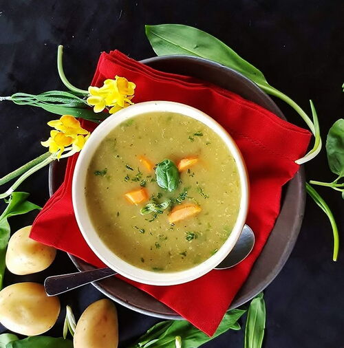Frische Wildkräutersuppe aus Alpenampfer, angerichtet mit Brot und Kräuterdeko.
