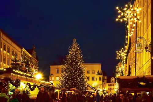 Christkindlmarkt in der Adventszeit: Verkaufsstände mit weihnachtlichen Dekorationen, Kunsthandwerk und regionalen Spezialitäten, umgeben von festlicher Beleuchtung und einer historischen Kulisse.