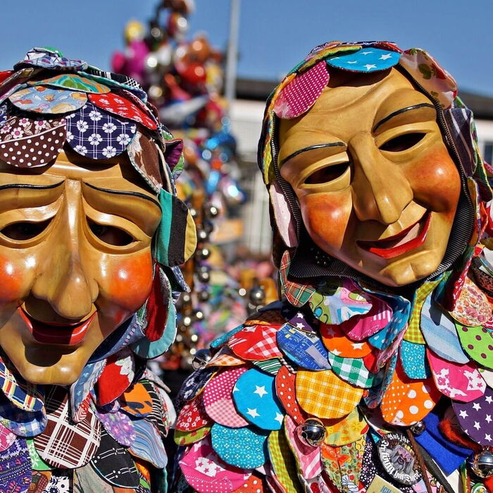 Fröhlicher Faschingsumzug mit maskierten Teilnehmern, die Süßigkeiten verteilen, und einer festlichen Atmosphäre voller Farben und Lachen.