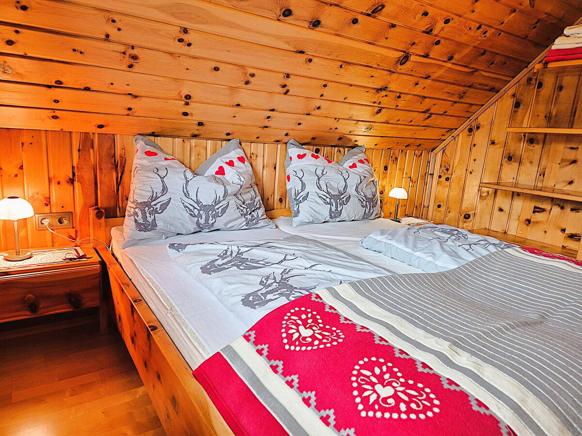 Doppelbett mit herzgemusterter Decke und Zirbenwänden im Schlafzimmer der Pietschacher Almhütte