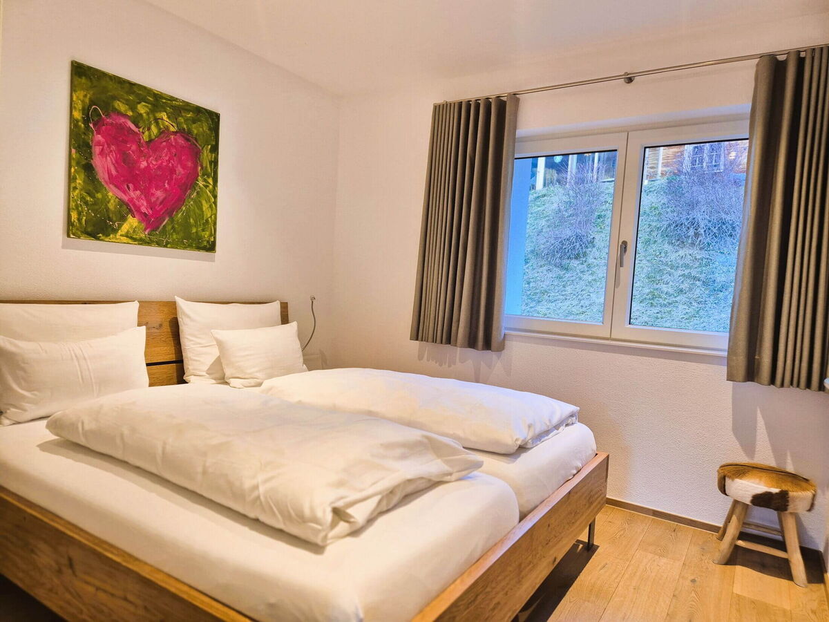 Second bedroom with a reclaimed wood double bed and a window onto the greenery in the Alpenglück luxury lodge Widderstein in the Kleinwalsertal
