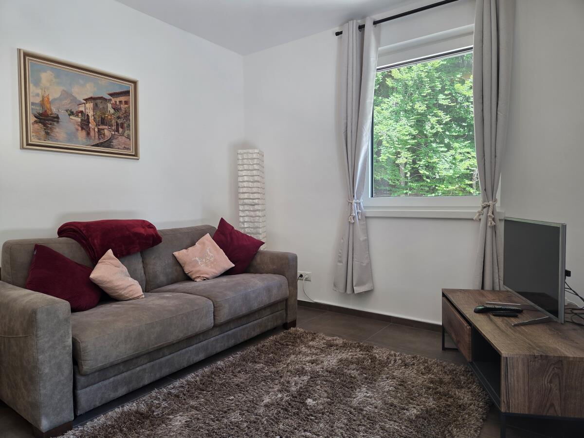 Wohnraum mit Sofa, Fernseher und Fenster ins Grüne in der Pferdeheimat am Karwendel in Gnadenwald, Ferienwohnung am Pferdehof für zwei bis drei Personen