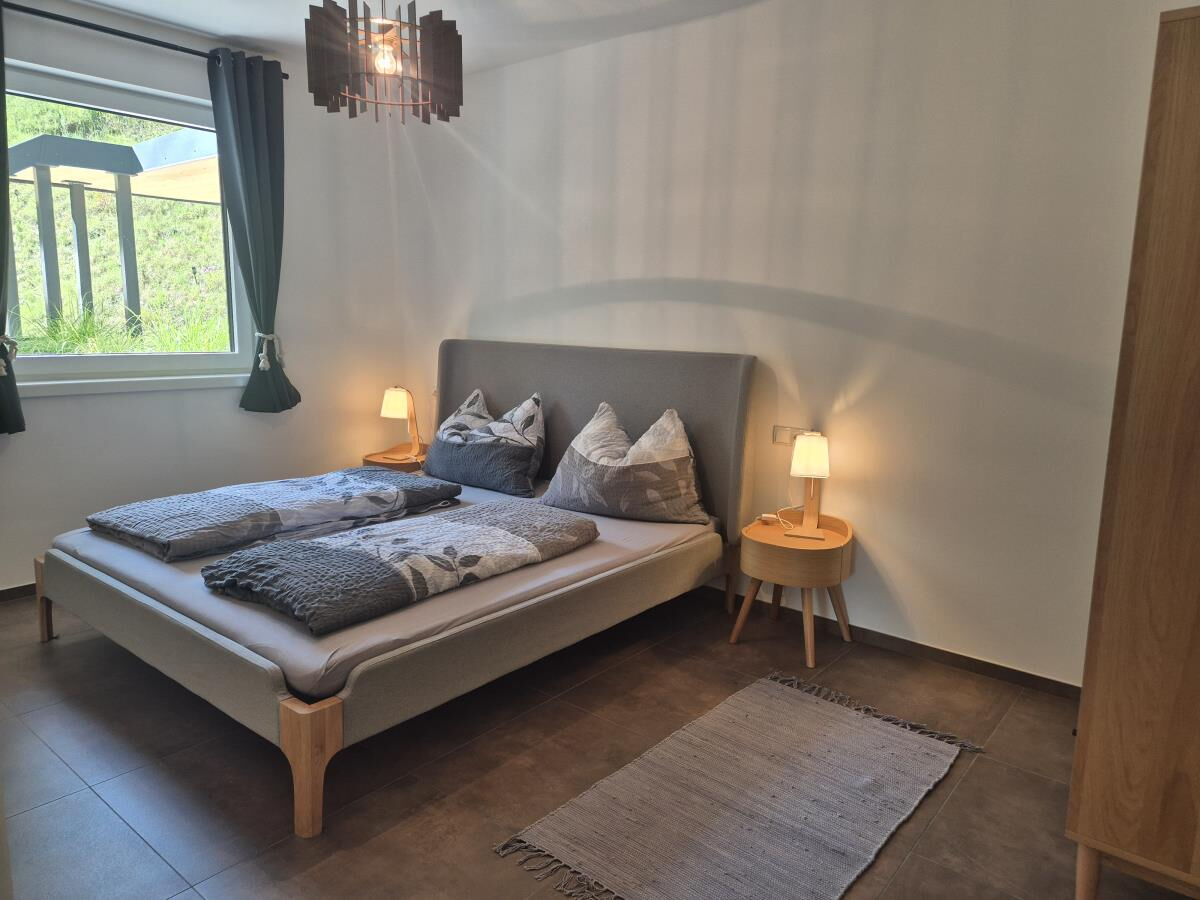 Bedroom of the Waldsicht holiday apartment near the Karwendel with double bed, bedside lamps and a window facing the greenery