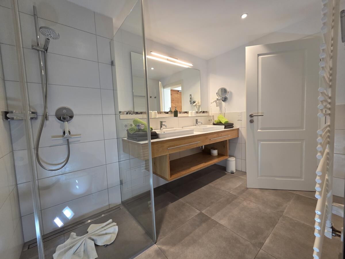 Badezimmer mit bodengleicher Glasdusche und Doppelwaschtisch aus Holz in der Garten-Luxuslodge Hammerspitze, Luxuslodge für 6 Personen im Kleinwalsertal