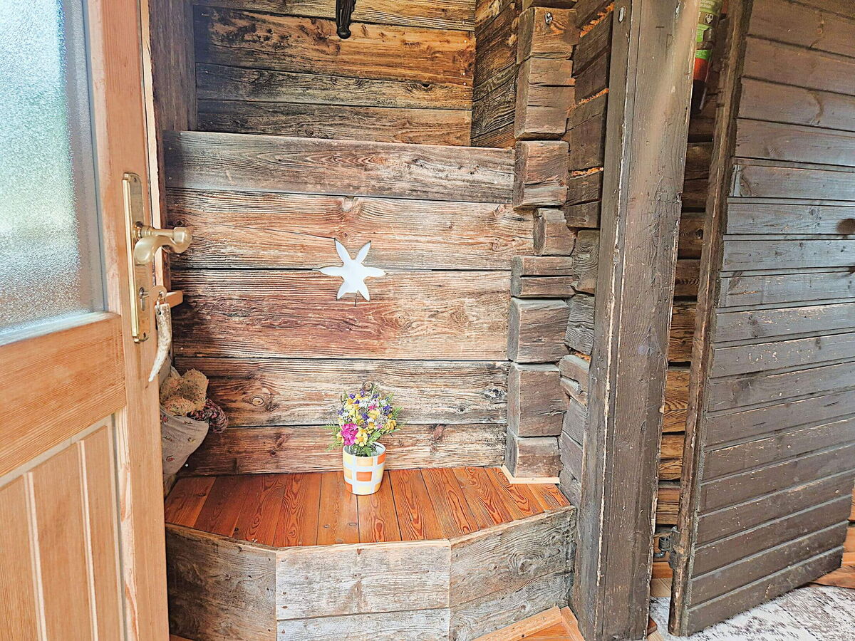Alte Holztür im Eingang der Pietschacher Almhütte mit geschnitztem Edelweiß und Blumen auf dem Baumstamm