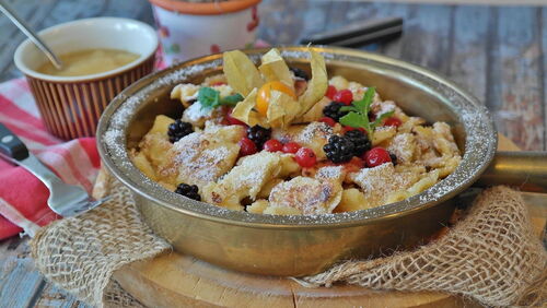 Ein Kaiserschmarrn in einer goldenen Pfanne mit verschiedenen Beeren und Minzblättern liebevoll angerichtet.