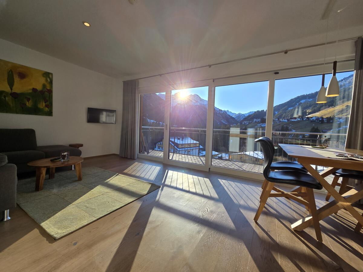 Living and dining area with sofa, dining table and balcony front in the Sonnenbalkon luxury lodge Bärenkopf, 70 square metres for up to six people