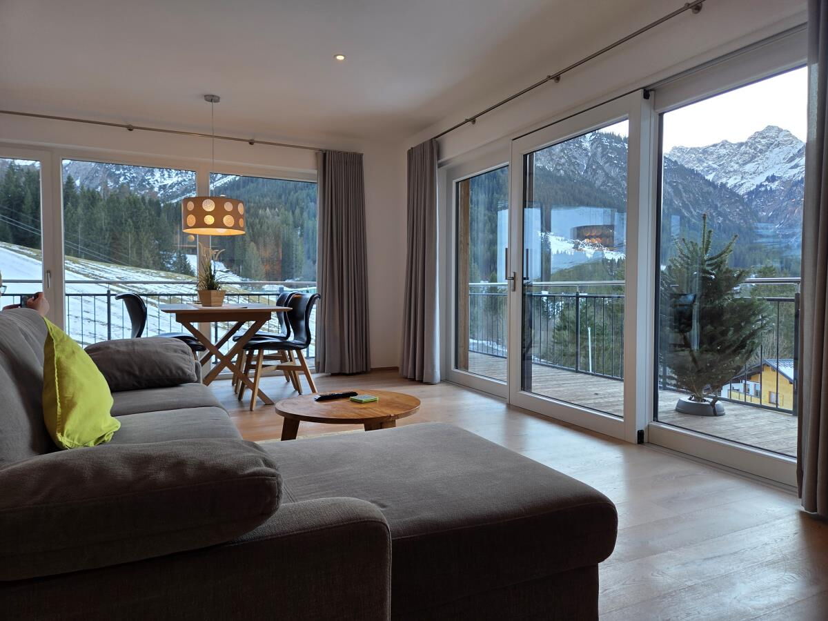 Living area with sofa, dining table and floor-to-ceiling windows onto the corner balcony in the Sonnenwende luxury lodge Elferkopf, holiday apartment for six people in the Kleinwalsertal