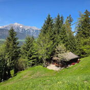 Das Kochhäusl am Wattenberg auf der Bergwiese zwischen Bäumen mit Blick auf das verschneite Karwendel, Berghütte in Alleinlage für zwei bis vier Personen