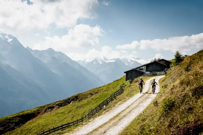 Two mountain bikers on the gravel track by the alpine hut, glaciated peaks behind