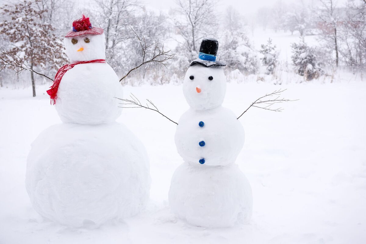 Zwei Schneemänner mit Hut und Schal stehen im tiefen Schnee vor der winterlichen Landschaft