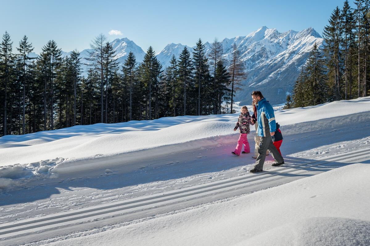 Familie beim Winterspaziergang auf dem geräumten Weg durch die verschneite Landschaft in den Tuxer Alpen, Winterurlaub am Kolsassberg