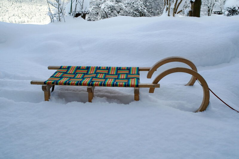 Old wooden sledge standing in deep snow in front of snow-covered trees at the Hochrindl