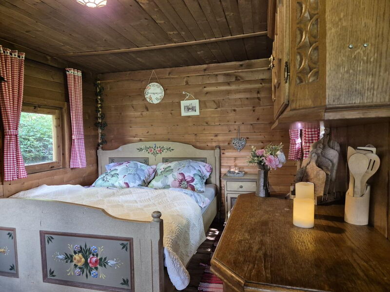 Schlafzimmer im Waldhüttl in Terfens mit Holzbett, hellerr Decke und handbemalter Tiroler Einrichtung.
