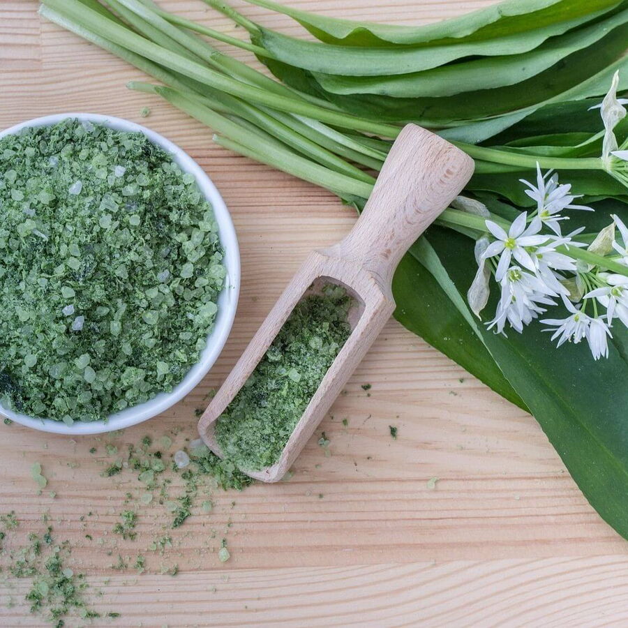 Frische Bärlauchblätter neben einem Glas selbstgemachtem Bärlauchsalz, angerichtet auf einem rustikalen Holztisch.
