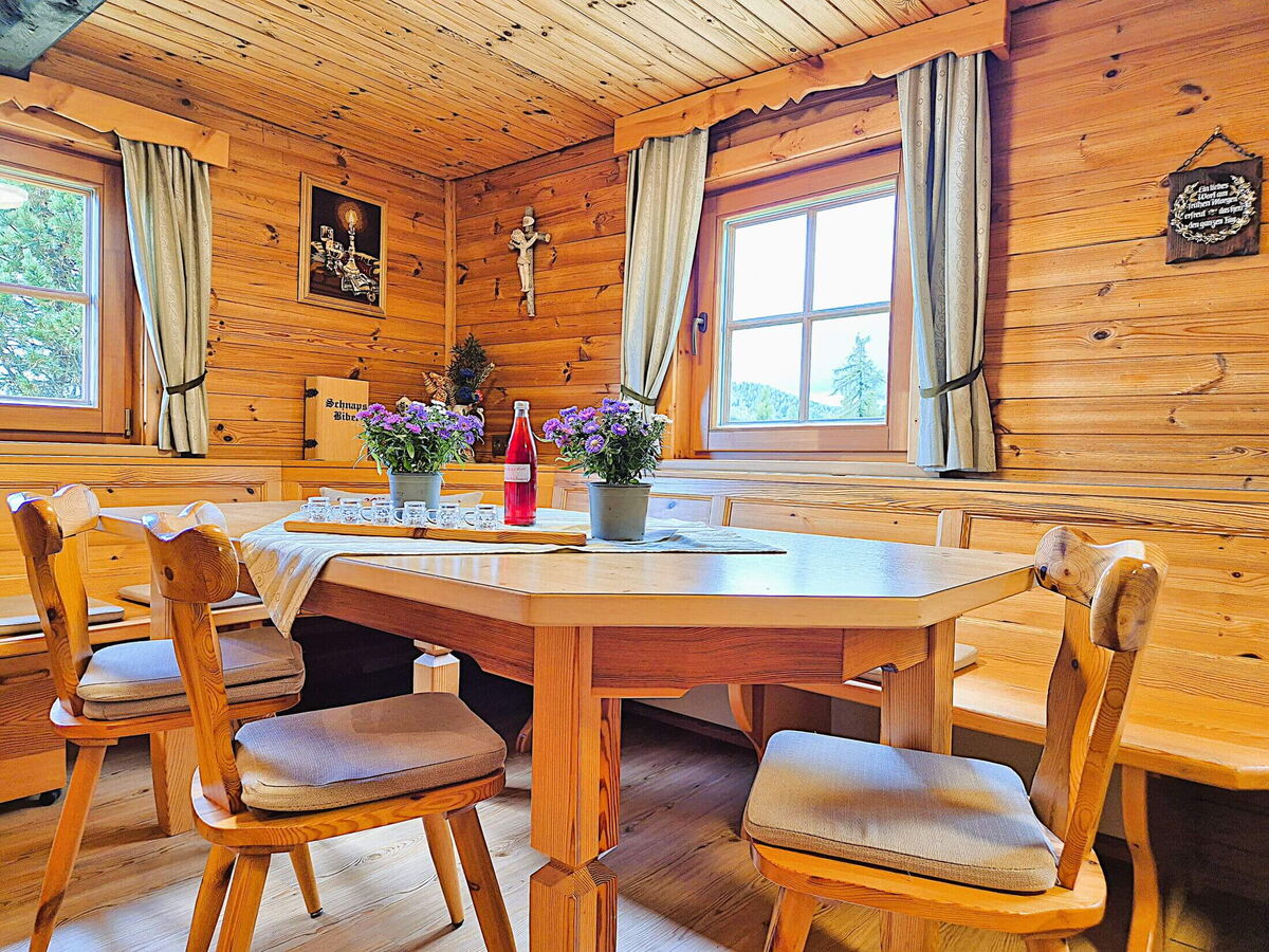 Esstisch der Pietschacher Almhütte mit Blumen und Flasche, Stühlen und Eckbank vor Zirbenwänden
