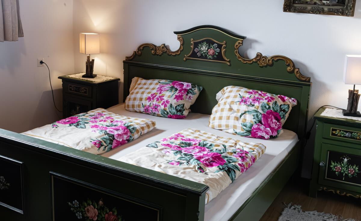 Bedroom in the Grafenhäusl with a green painted farmhouse bed and floral linen, holiday house in Tyrol