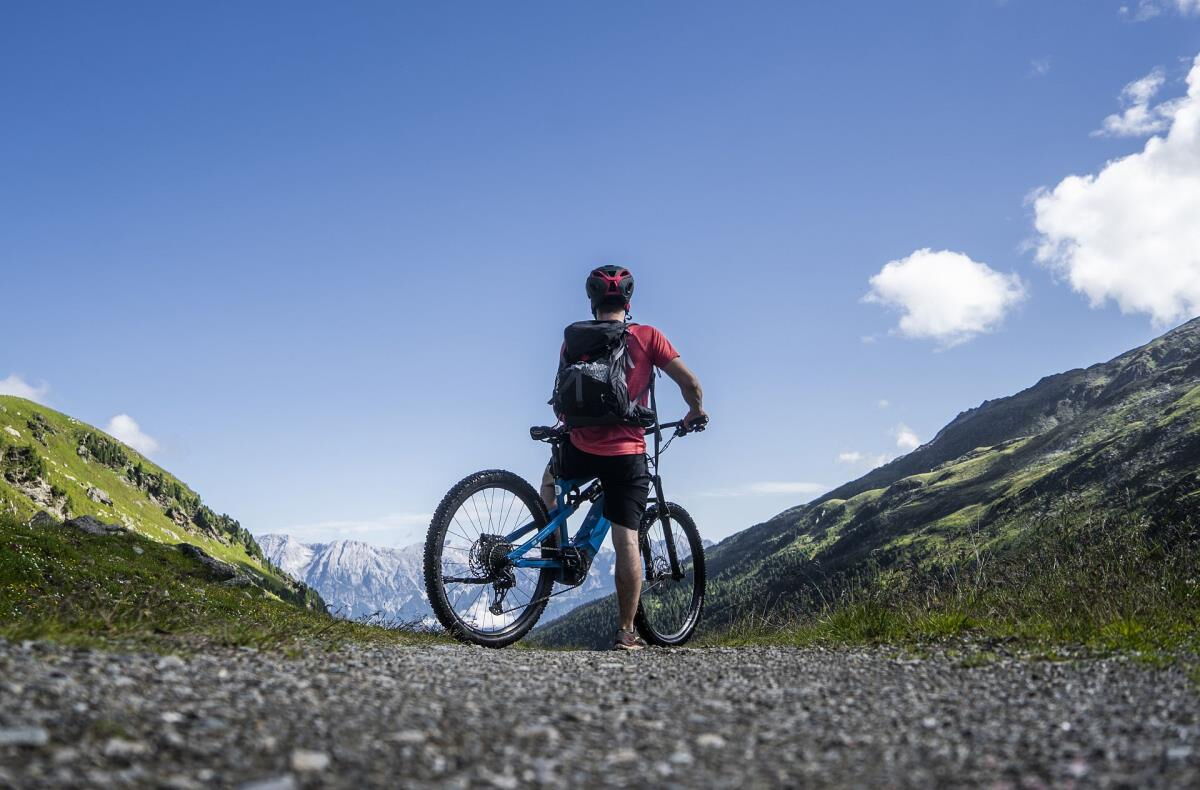 Mountainbiker steht auf der Bergstraße und schaut über das grüne Tal in Tirol