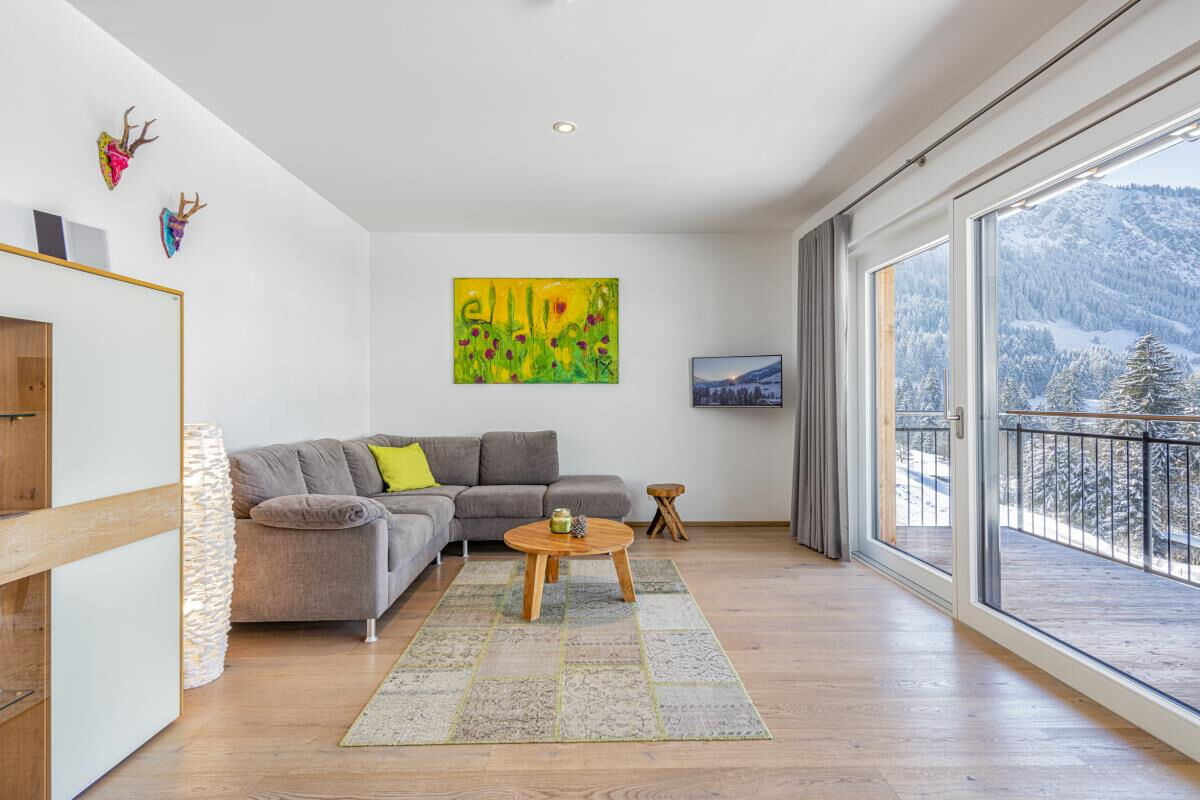 Bright living area with sofa and floor-to-ceiling panorama window in the Alpenglück luxury lodge Widderstein, holiday apartment for families and friends in Mittelberg in the Kleinwalsertal