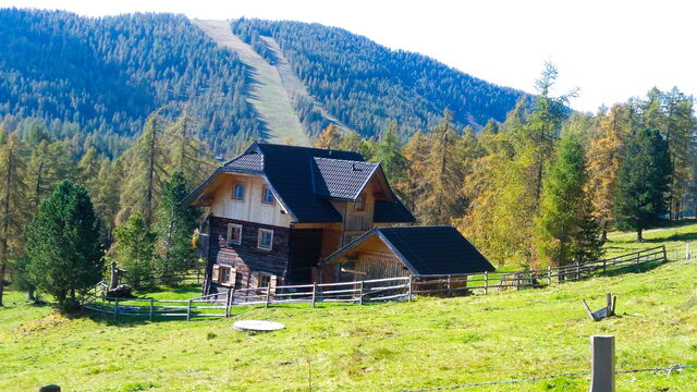 Die Pietschacher Almhütte im Herbst auf der Almwiese, dahinter die Trasse der Skipiste am Hochrindl