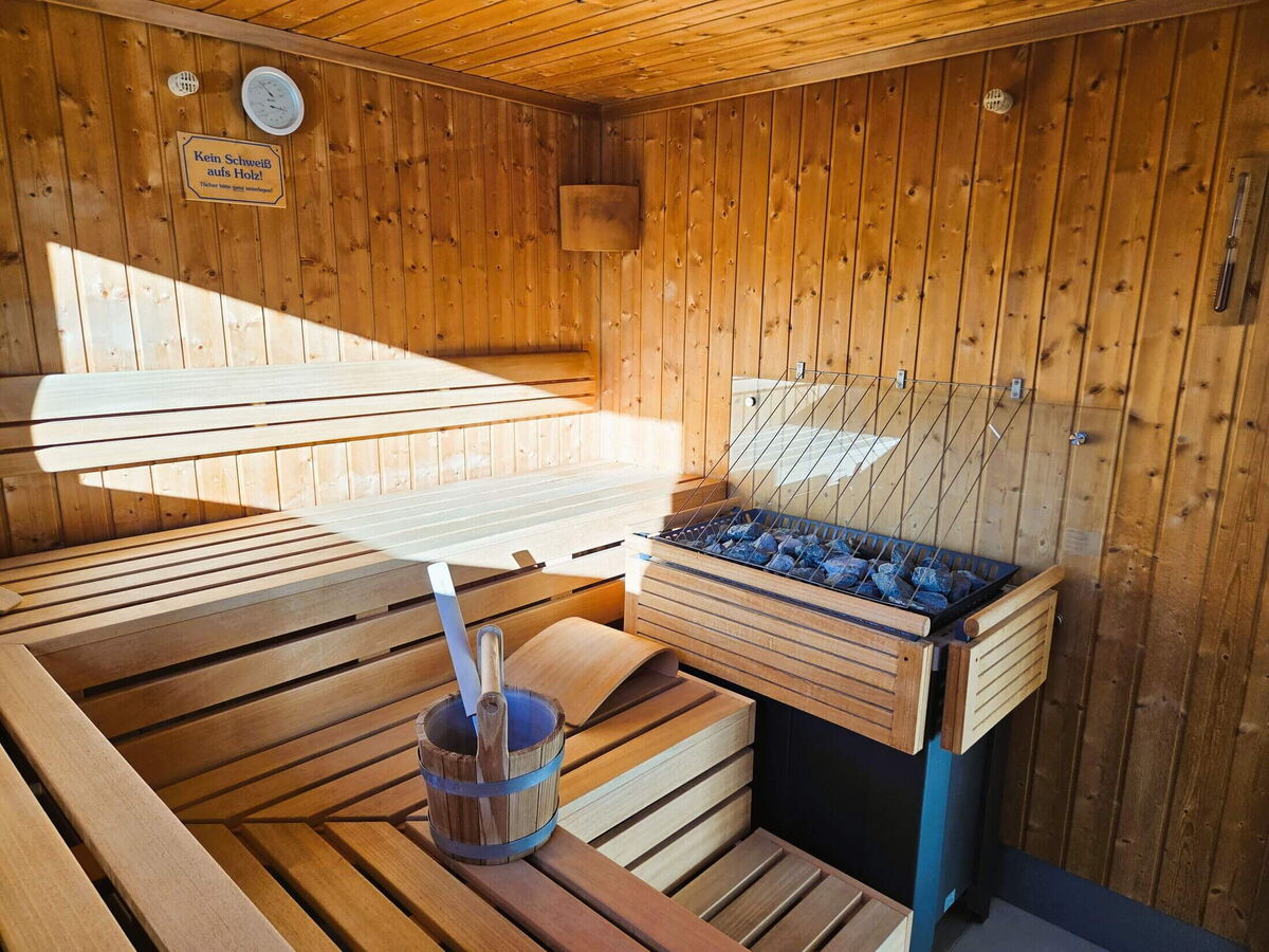 Sauna stove with hot stones and a wooden infusion bucket in the panorama sauna of the Walser Lodge in the Kleinwalsertal