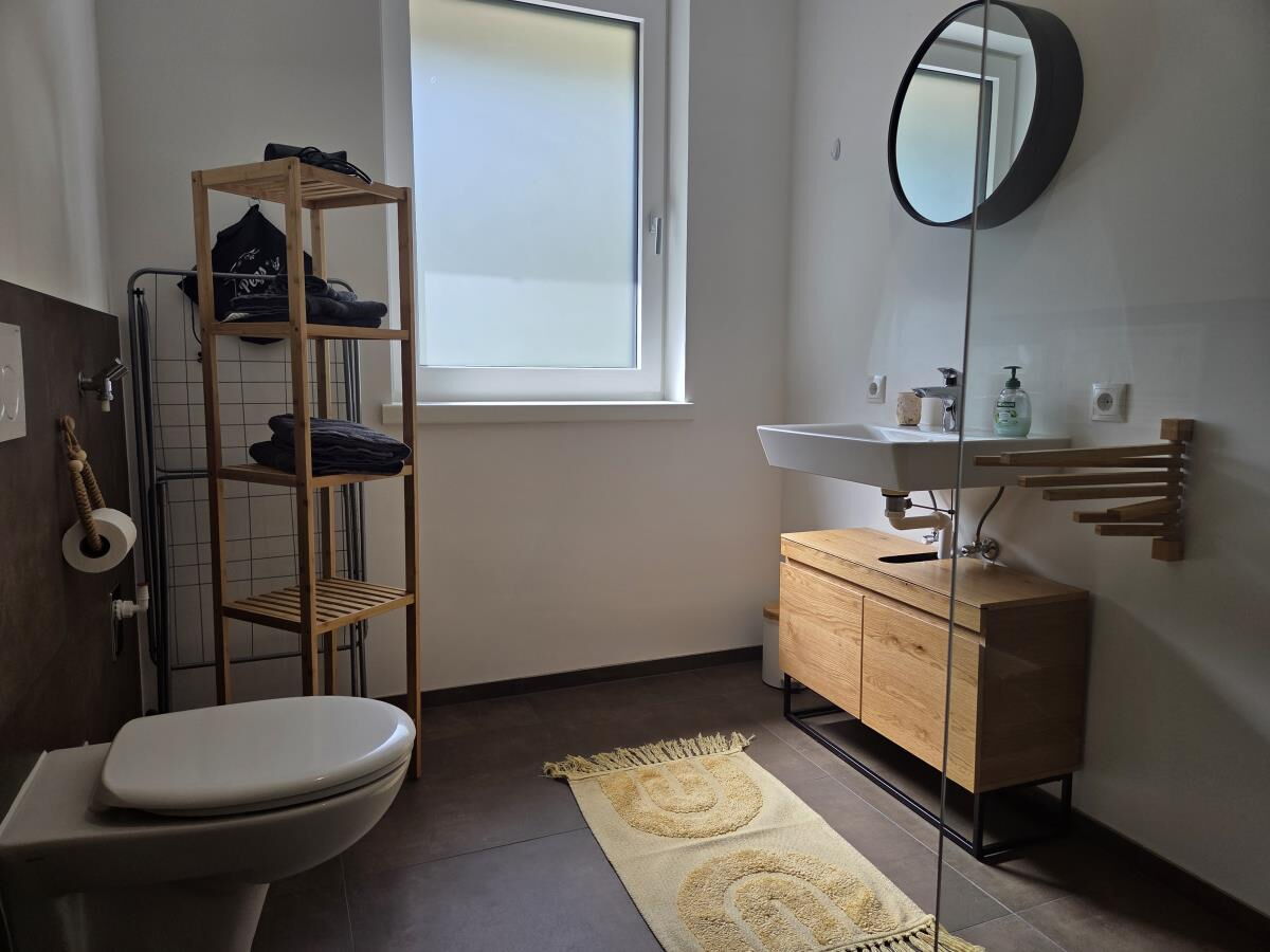 Bathroom of the Waldsicht holiday apartment with WC, wooden washstand, round mirror and window