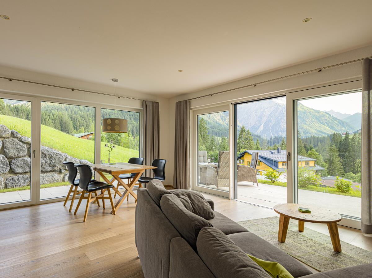 Wohnraum mit Sofa, Esstisch und Fensterfront zur Sonnenterrasse in der Garten-Luxuslodge Hammerspitze, Luxuslodge für 6 Personen im Kleinwalsertal