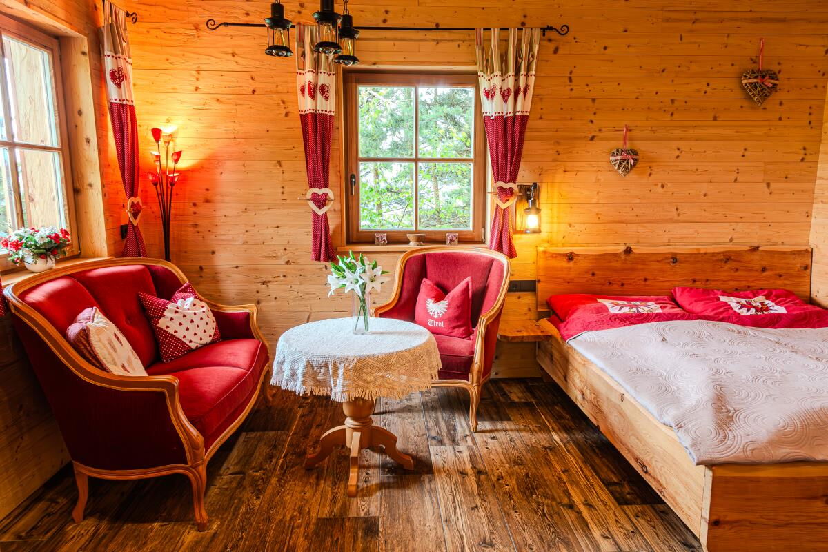 Swiss pine bed next to the seating corner with red armchairs in the Tiroler Hütte near the Karwendel range, chalet for two people