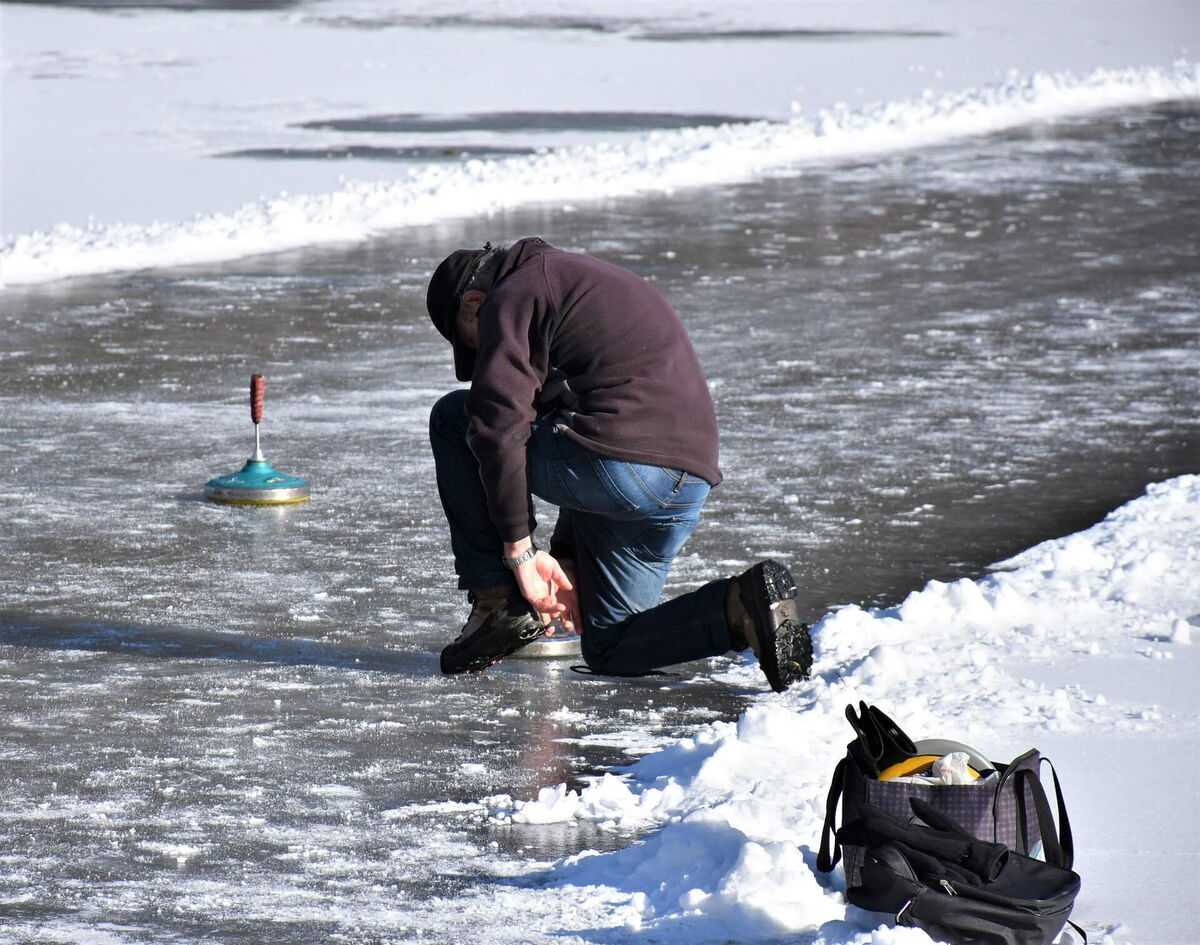 Mann kniet beim Eisstockschießen auf dem zugefrorenen See und setzt seinen Eisstock auf das Eis